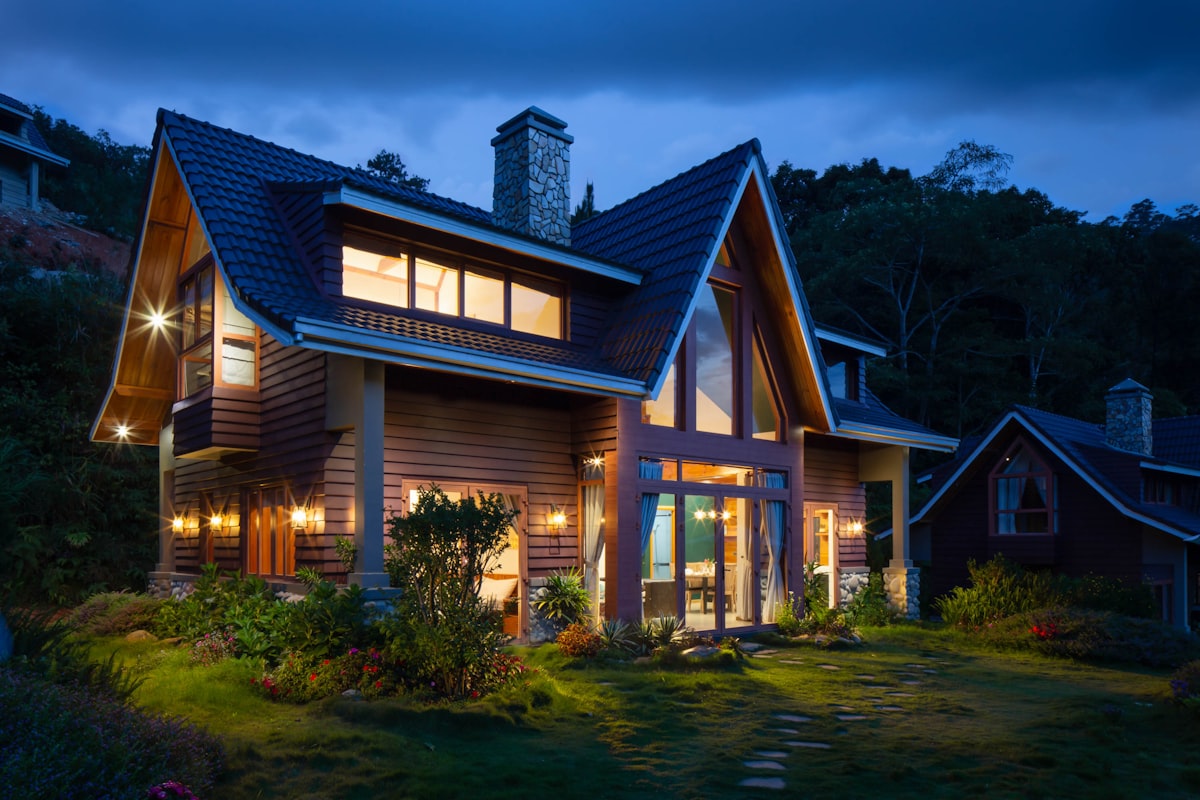 House with a steep roof and lit windows at dusk, surrounded by trees (sample photo)